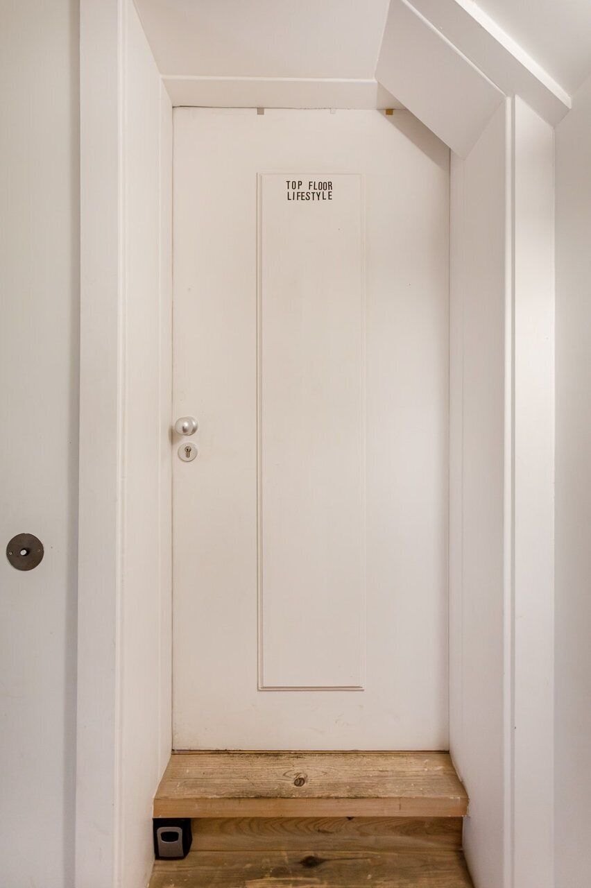 Een witte deur met een bord waarop 'TOP FLOOR LIFESTYLE' staat, en een houten trap die erheen leidt.