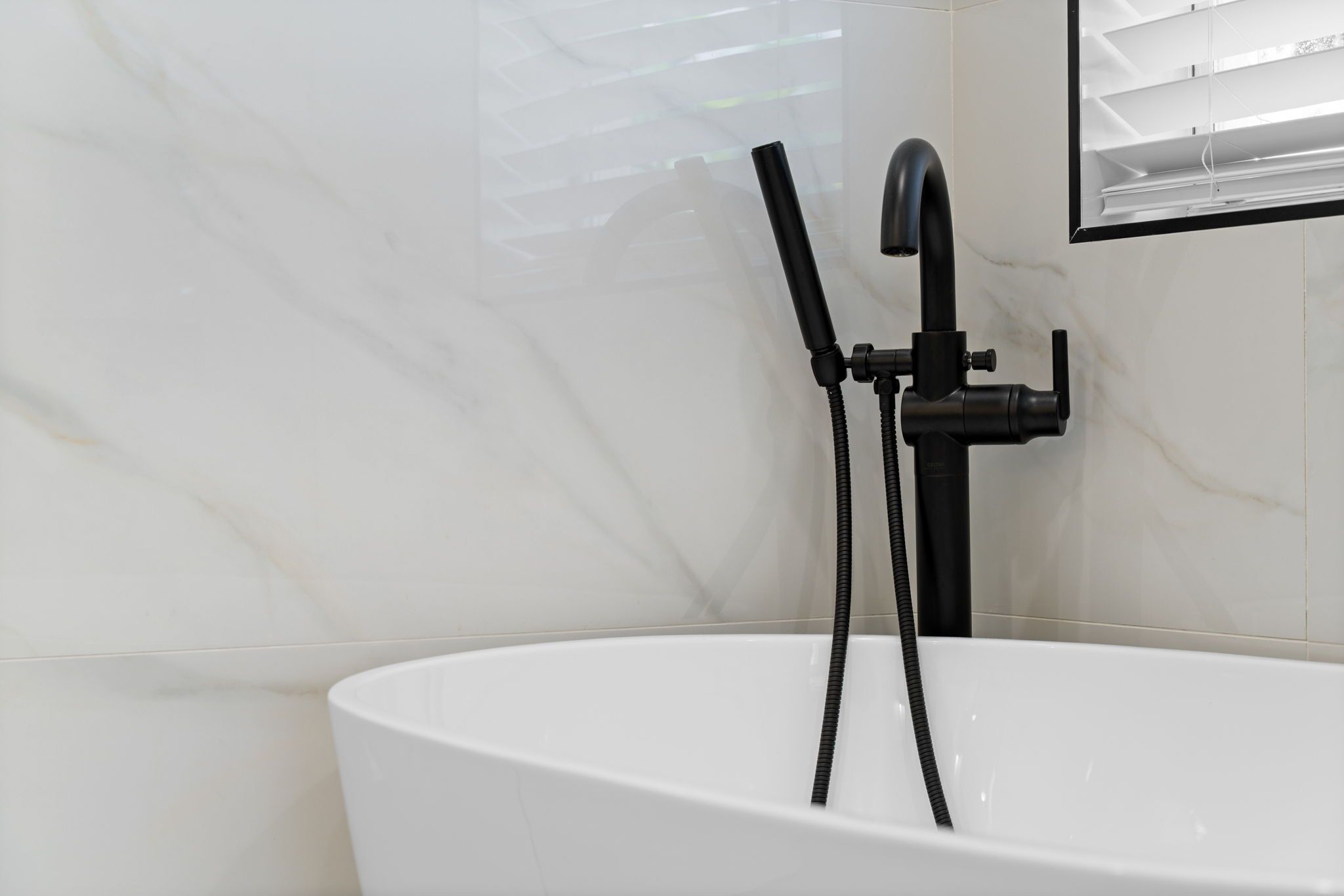 A modern bathroom with a white bathtub, black shower fixtures, and a window with blinds.