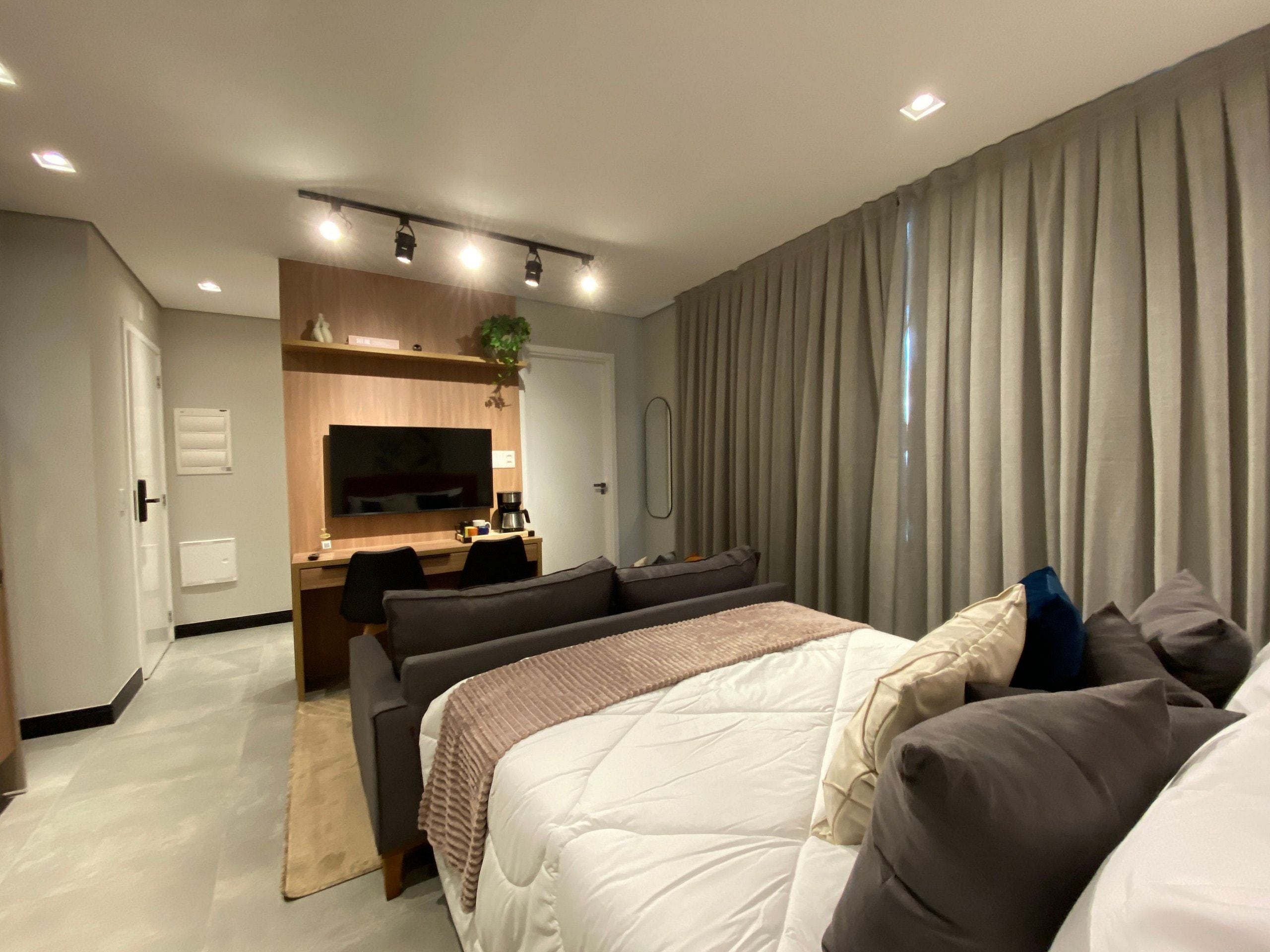 A modern hotel room with a bed, a desk, a TV, and a large window with curtains.