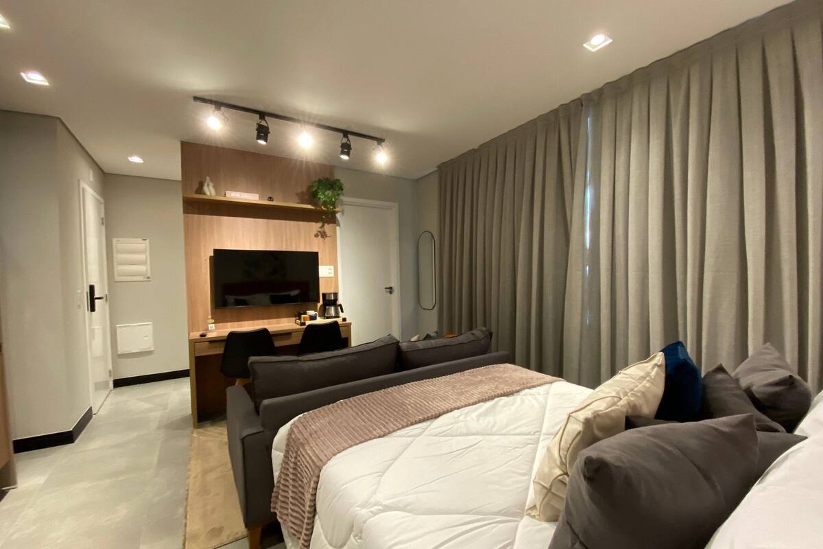 A modern hotel room with a bed, a desk, a TV, and a large window with curtains.