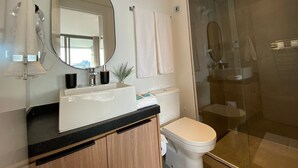 Un baño moderno con cabina de ducha de vidrio, inodoro blanco y tocador con espejo y lavamanos.