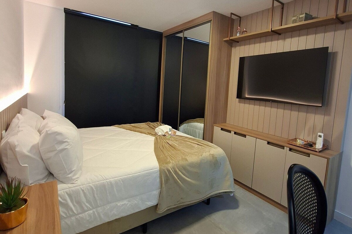 Un dormitorio moderno con cama, mesita de noche, silla, televisor y armario.