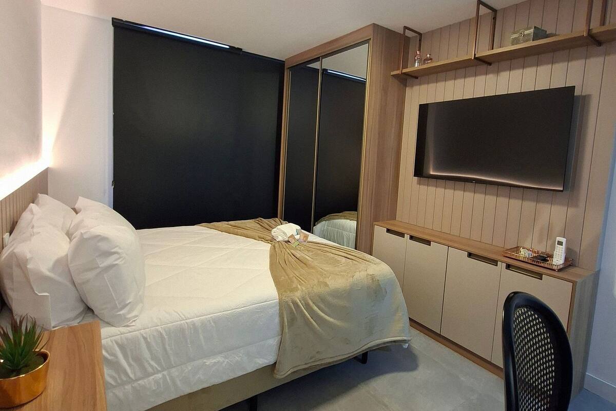 A modern bedroom with a bed, bedside table, chair, TV, and wardrobe.