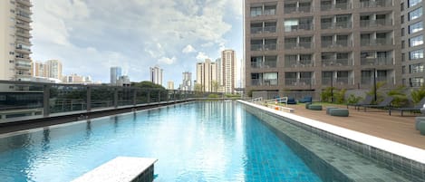 Una piscina con solárium empedrado, rodeada de edificios altos.