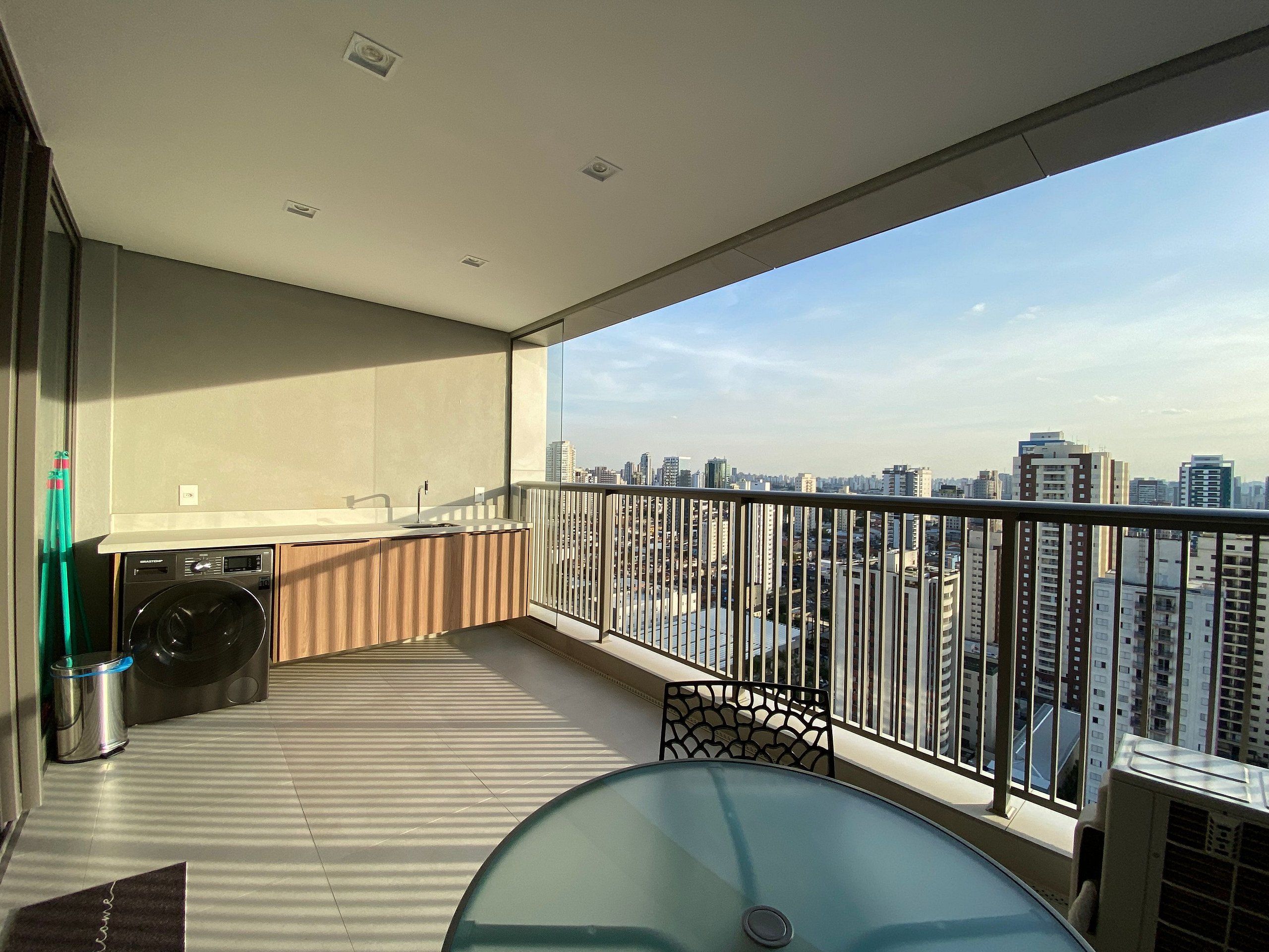 A balcony with a washing machine, a table, and a view of a cityscape.