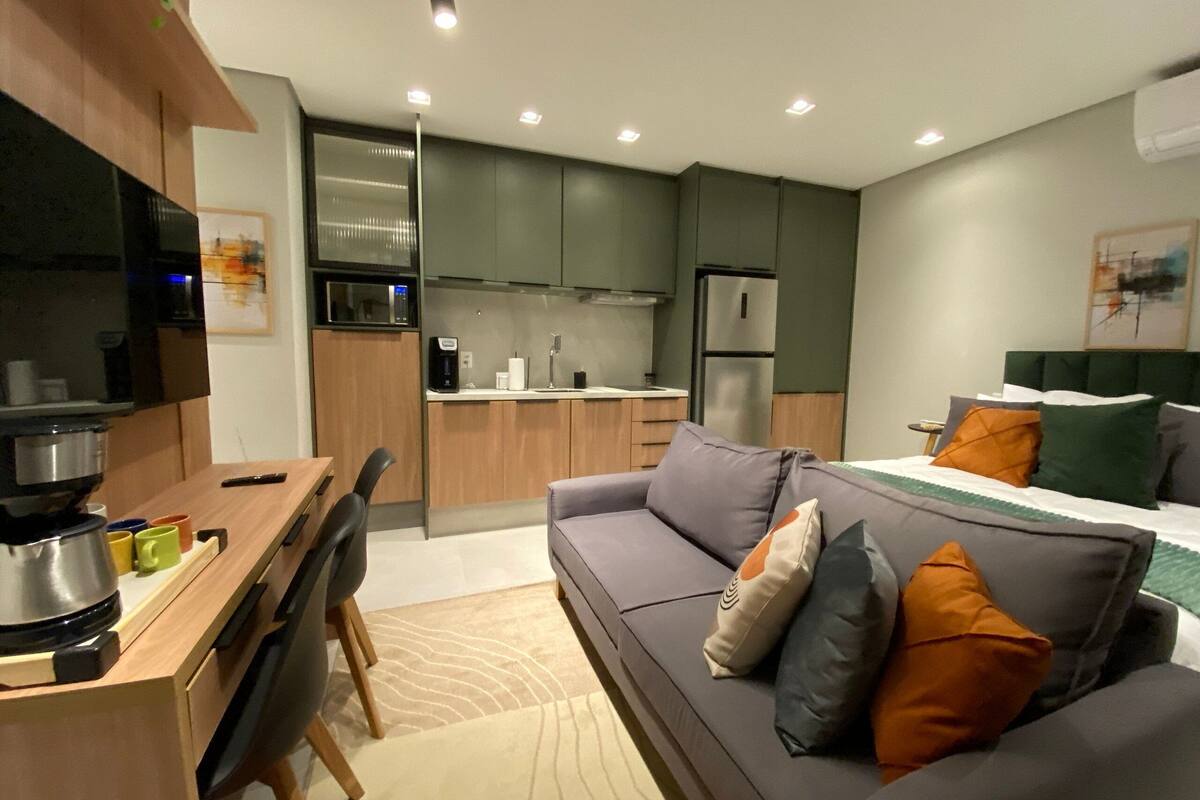 A compact living space with a kitchenette, a sofa with cushions, a dining table with chairs, and a bed with pillows.
