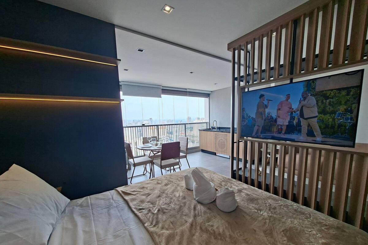 A bedroom with a bed, a TV, and a balcony with a view.
