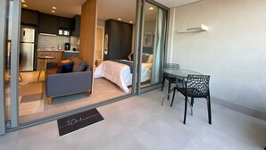 A modern hotel room with a glass door leading to a kitchenette, a bed with a white duvet, a small table with chairs, and a 'Welcome' mat. - Estúdios com piscina no lounge (São Paulo)