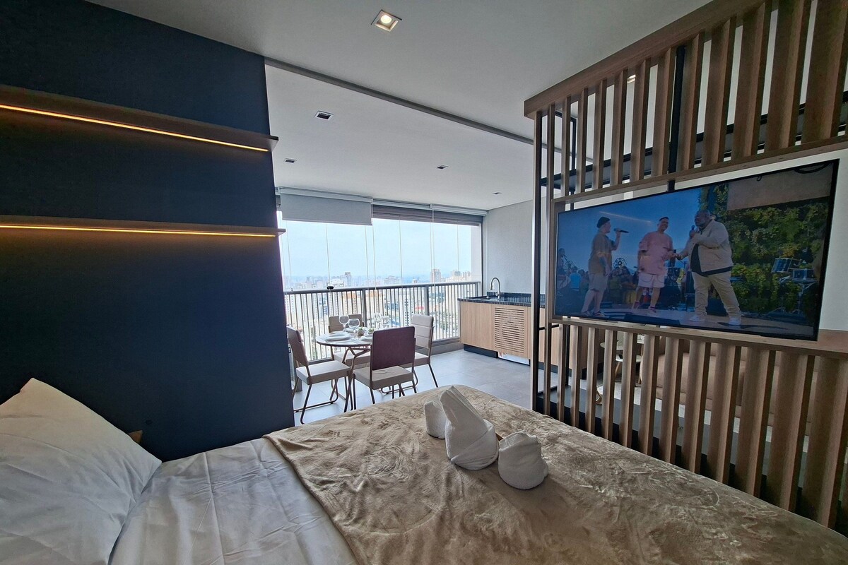 Un dormitorio con cama, televisor y balcón con vistas.