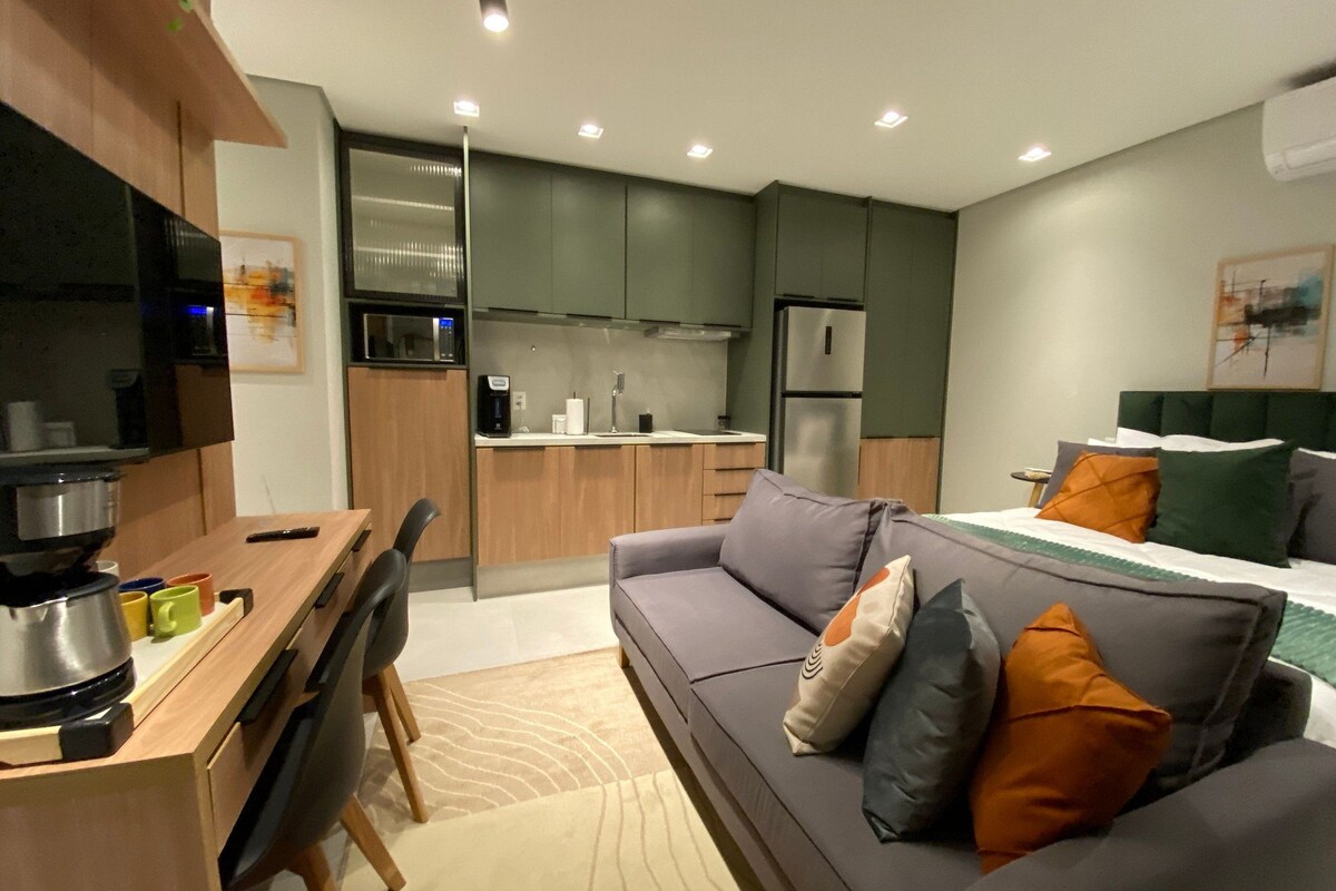Un espacio habitable compacto con kitchenette, un sofá con cojines, una mesa de comedor con sillas y una cama con almohadas.