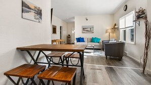 En matplats med ett träbord och bänkar, en soffa med kuddar, en lampa och ett fönster med persienner.