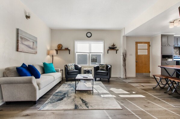 A spacious living room with a sofa, coffee table, and a view of the kitchen. - Oconto Hideaway- Mid/Long term stays welcome! (Oconto)