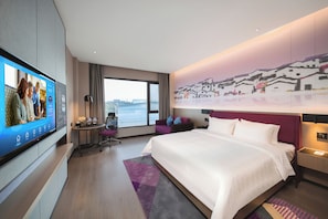 Une chambre d’hôtel moderne dotée d’un grand lit, d’un téléviseur mural, d’un bureau et offrant une vue sur la ville.