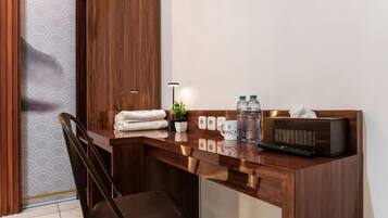 A hotel room with a wooden desk, a chair, a remote control, a radio, and a small potted plant.