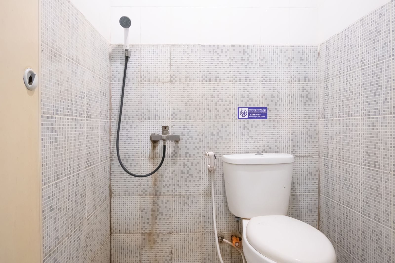 Een kleine badkamer met toilet, douche en een bordje met de tekst: geen etensresten doorspoelen.