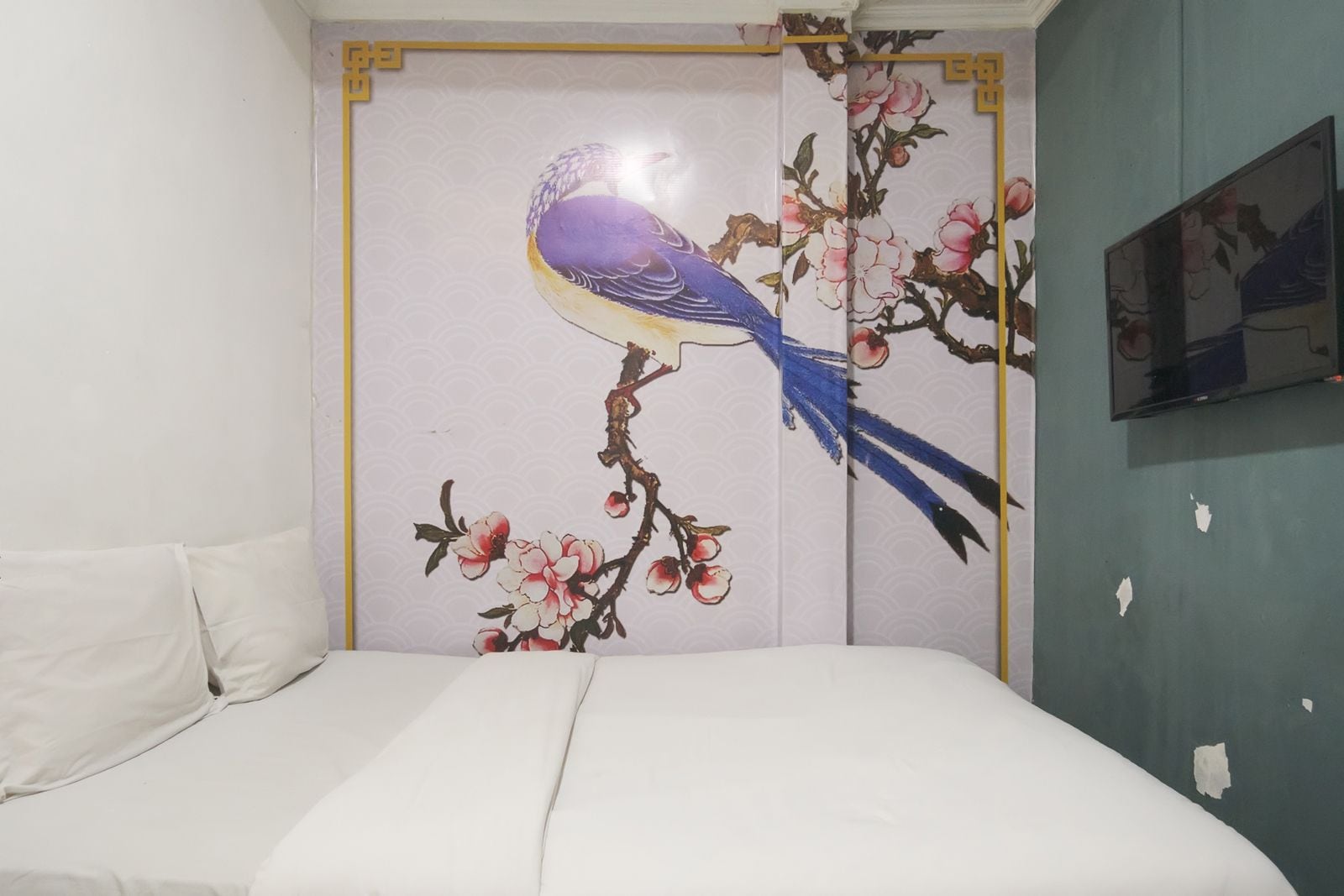 Ein Schlafzimmer mit einem Bett, einer Wand mit einem Blumenbild und einem teilweise sichtbaren Fernseher.