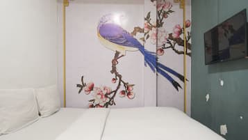 Ein Schlafzimmer mit einem Bett, einer Wand mit einem Blumenbild und einem teilweise sichtbaren Fernseher.