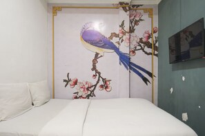 Ein Schlafzimmer mit einem Bett, einer Wand mit einem Blumenbild und einem teilweise sichtbaren Fernseher.