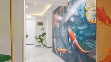 Un pasillo con un gran mural de peces koi, una planta en maceta y una puerta con una franja amarilla.