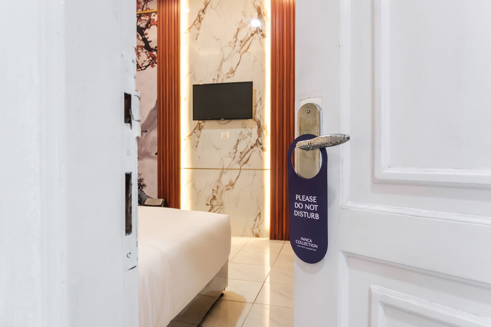 Habitació d'hotel amb un llit, una televisió penjada a la paret i una porta amb un cartell que diu 'NO MOLESTAR'.