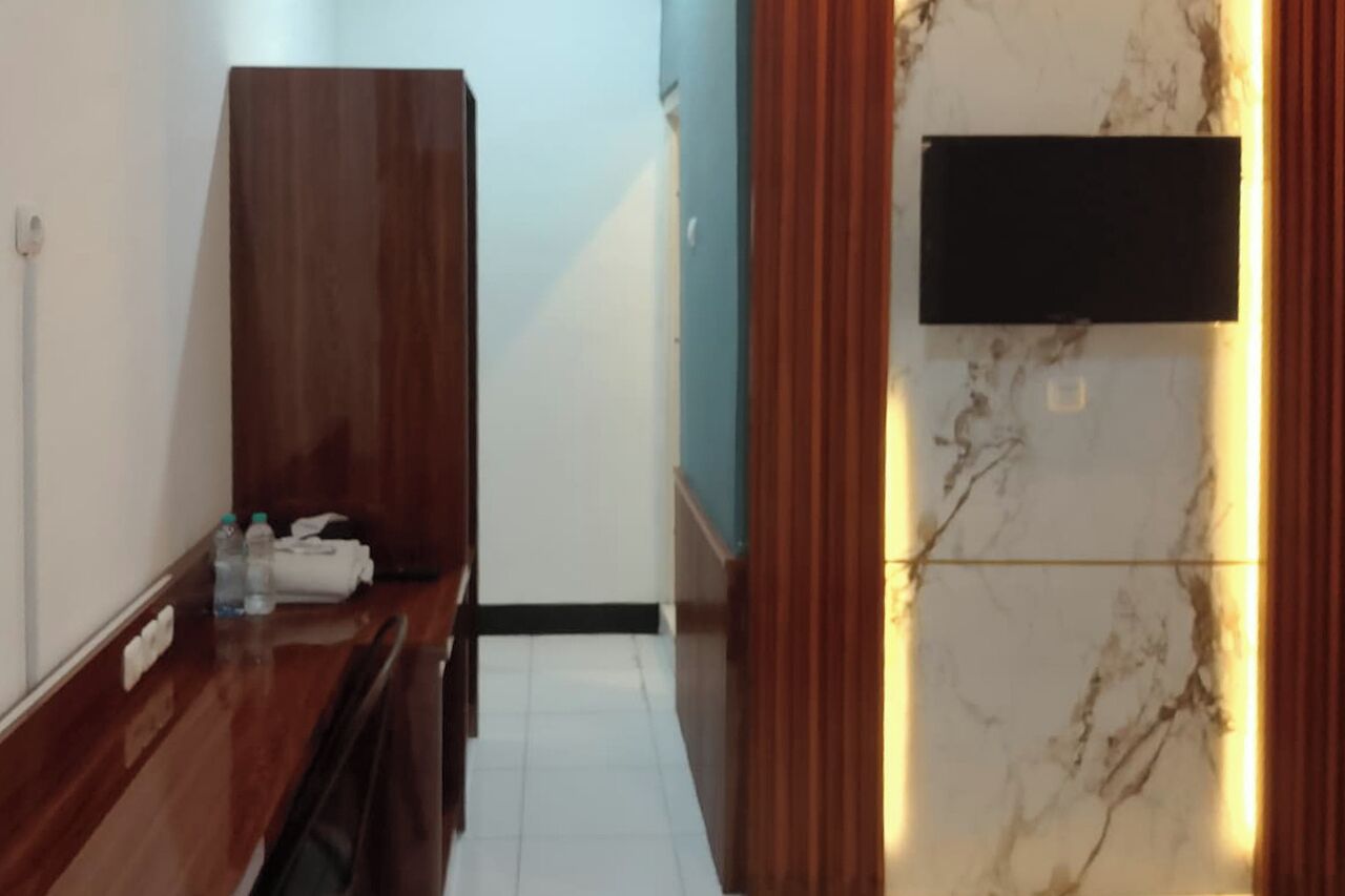A hotel room with a wooden desk, a flat-screen TV mounted on the wall, and a marble-patterned wall.