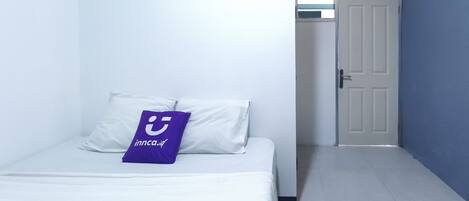 A hotel room with a bed, a pillow with a logo, a door, and a hallway.