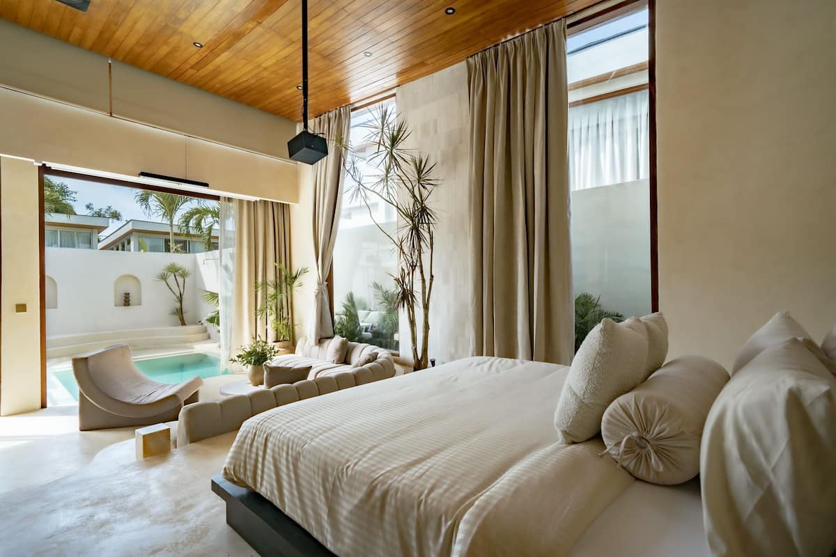 Une chambre moderne avec un grand lit, un fauteuil aux lignes arrondies et une vue sur une piscine et un espace extérieur.