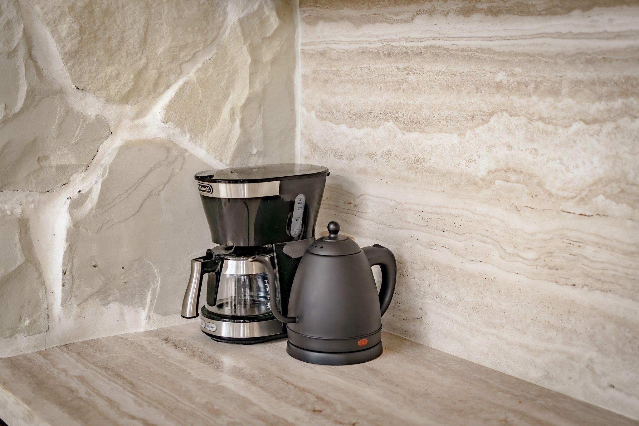 A coffee maker and a kettle on a marble countertop.