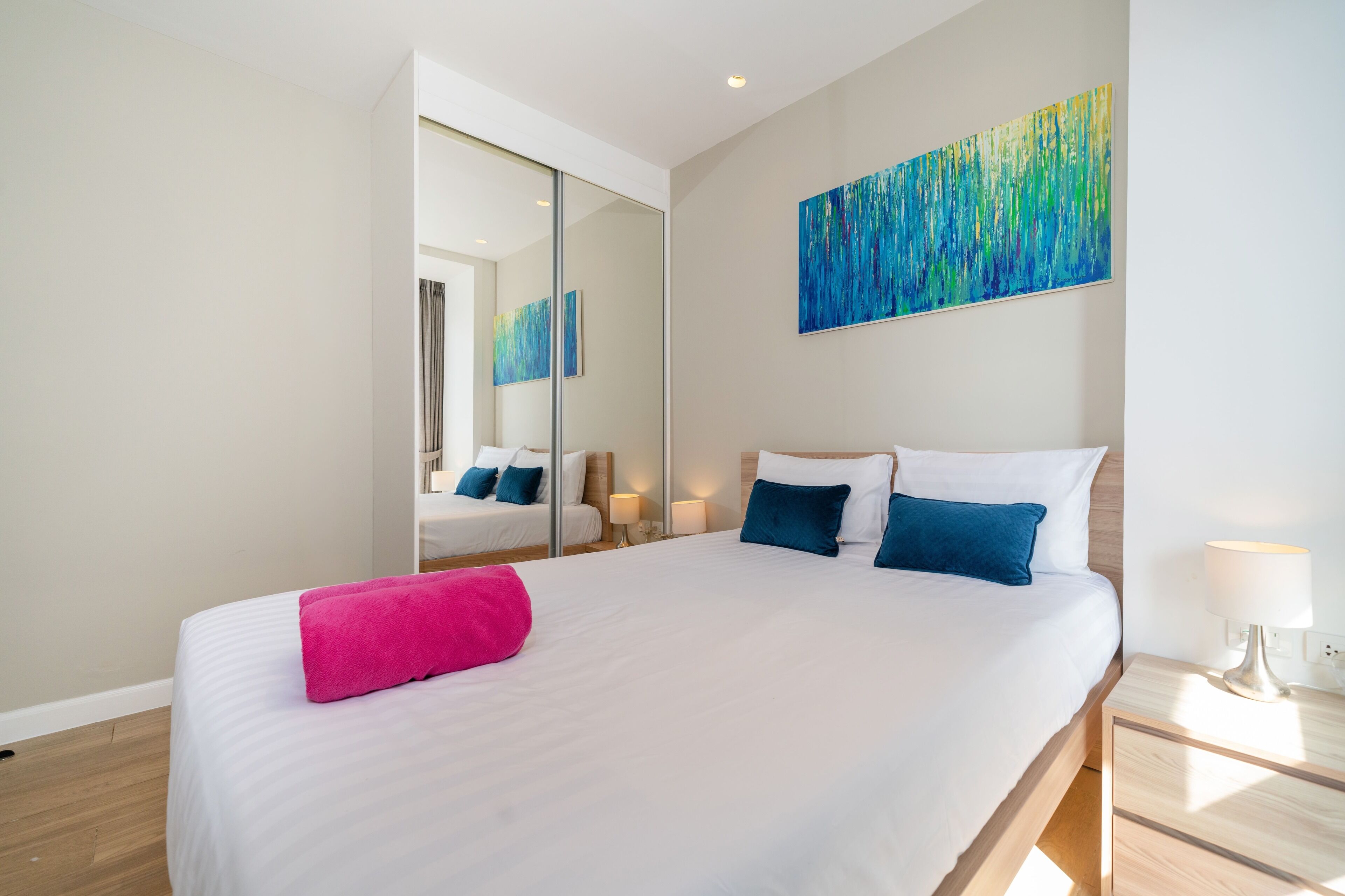 Una camera d'albergo moderna con un letto grande, uno specchio, un quadro e un comodino.