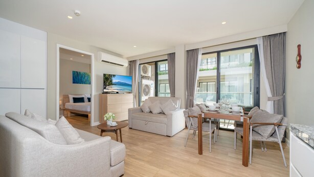 Ein modernes Wohnzimmer mit Sofa, einem Esstisch mit Stühlen und einer Küchenzeile mit Kühlschrank.