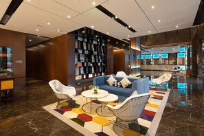 A modern lobby with a blue sofa, white armchairs, a round coffee table, and a colorful rug. - Hangzhou Canal Hampton by Hilton Hotel (Hangzhou)