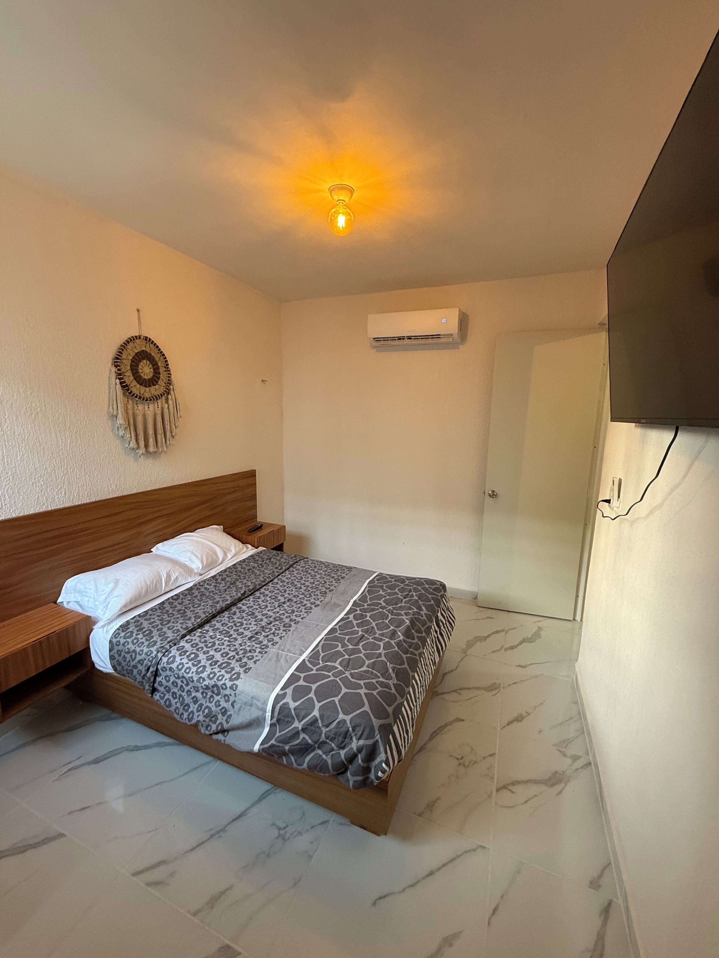 A bedroom with a bed, a wall-mounted air conditioner, a wall decoration, and a door.