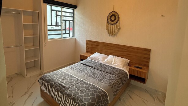 Ein Schlafzimmer mit Bett, Kleiderschrank, Nachttisch, Wandbild und Fenster mit Ausblick.