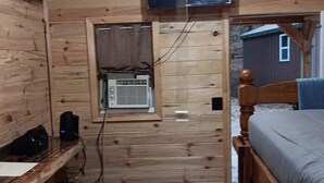 A compact wooden cabin room with a bunk bed, a desk with a chair, a small window, and a ceiling-mounted television. - Cozy 2-Person cabin in charming Parish with AC for relaxing stays (Parish)