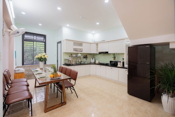 A modern kitchen with a dining area, equipped with a refrigerator, microwave, and various appliances. - Anh House (Da Nang)