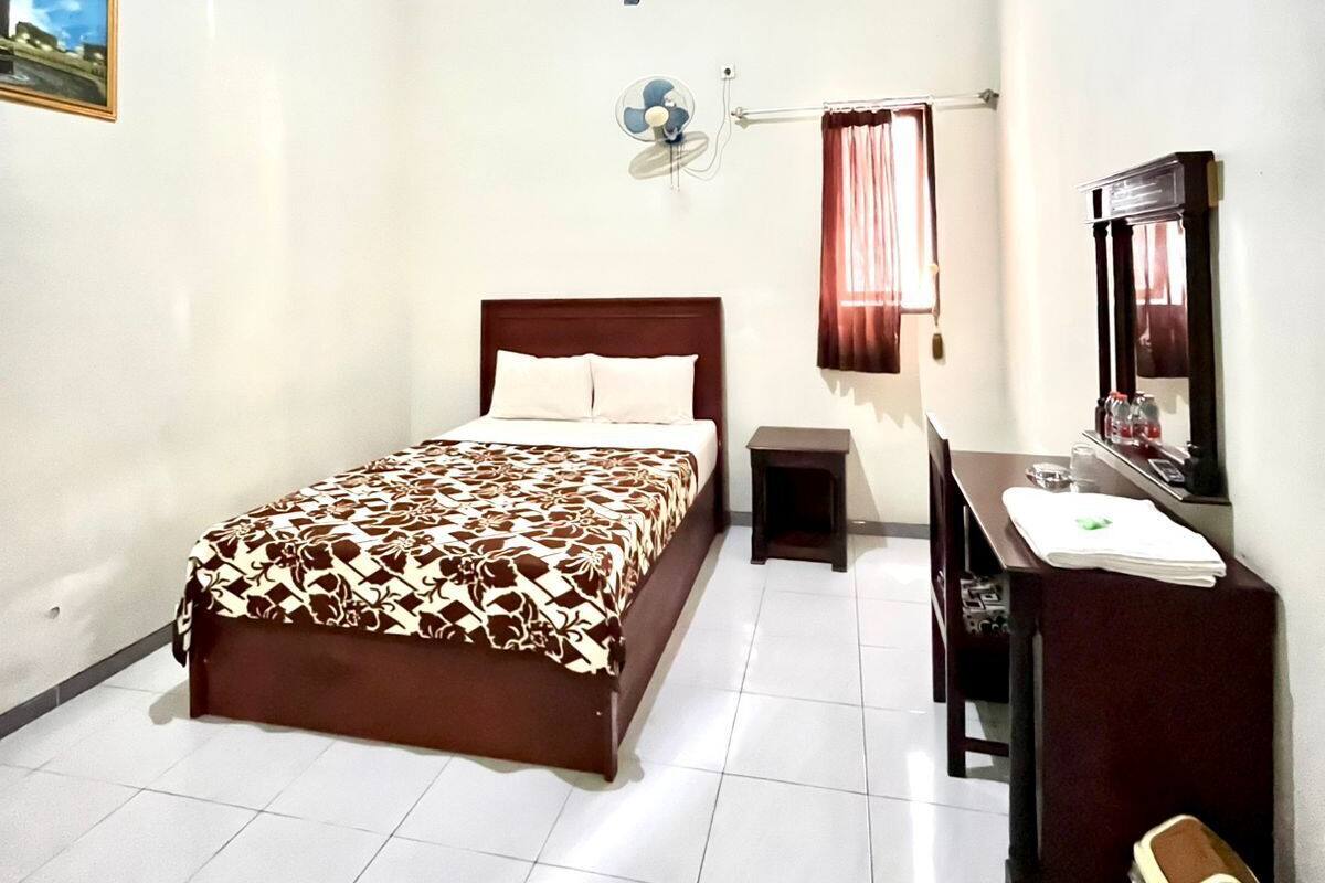 A bedroom with a bed, bedside table, mirror, and a small fan.