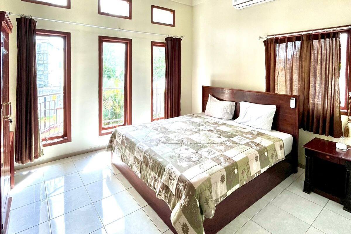 A spacious bedroom with a large bed, multiple windows, and an air conditioning unit.