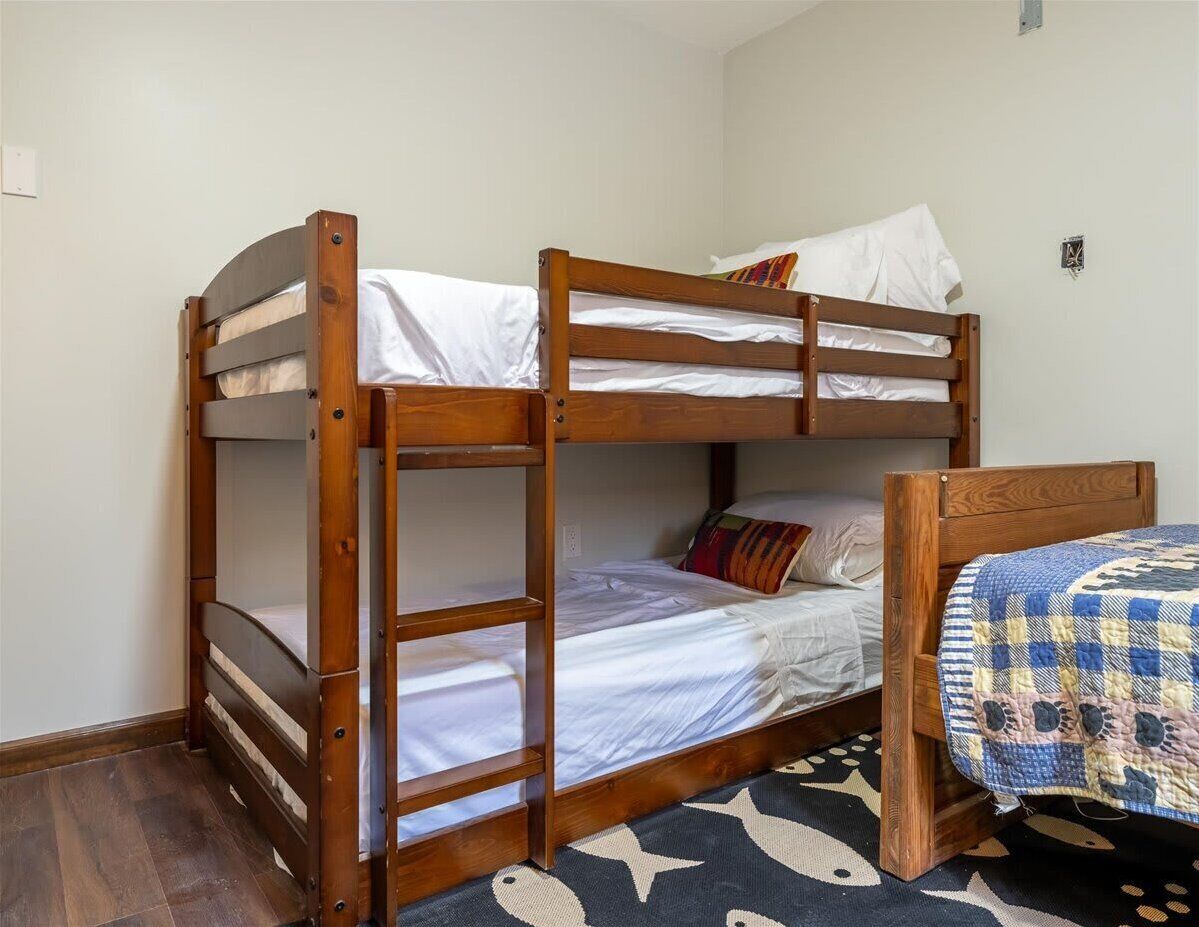 A bunk bed with a lower bunk and a single bed, a wooden headboard, and a patterned rug on the floor.
