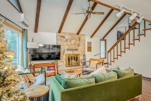 A modern living room with a stone fireplace, a large flat-screen TV, a green sofa, and a wooden staircase. - Tranquil Lake Harmony Spa Chalet, Hot Tub, Game Rm (Lake Harmony)