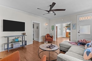 Ein modernes Wohnzimmer mit Flachbildfernseher, Deckenventilator, rundem Couchtisch und einem grauen Sofa.