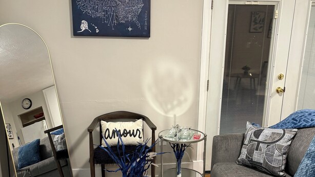 A living room with a glass coffee table, a sofa, a chair, a mirror, and a wall art piece. - Peaceful Hideaway 1-bedroom apartment with king bed in charming Belhaven (Jackson)