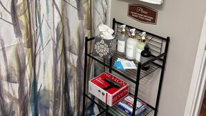 A bathroom with a shower curtain, a towel rack, a sign, a shelf with toiletries, and a Revlon box. - Peaceful Hideaway 1-bedroom apartment with king bed in charming Belhaven (Jackson)