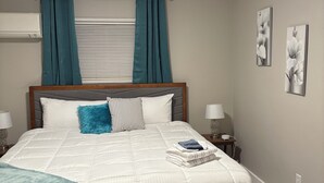 A neatly arranged bedroom with a bed, two bedside tables, a window with curtains, a ceiling light, and two wall-mounted artworks. - Peaceful Hideaway 1-bedroom apartment with king bed in charming Belhaven (Jackson)