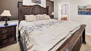 Une chambre à coucher avec un grand lit, une tête de lit en bois, deux tables de chevet avec des lampes, une commode et des œuvres d ’art accrochées aux murs.