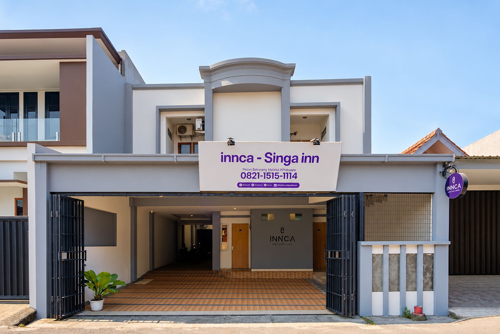 A modern hotel entrance with a signboard for INNCA - Singa Inn, featuring a contact number and WhatsApp booking option.