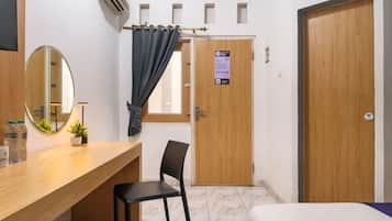 A hotel room with a wooden desk, a chair, a bed, a mirror, and a door with a sign.