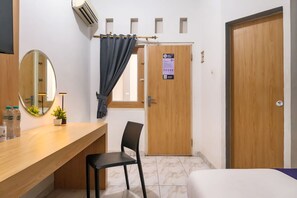 A hotel room with a wooden desk, a chair, a bed, a mirror, and a door with a sign. - INNCA Singa Utara, Semarang (Semarang)
