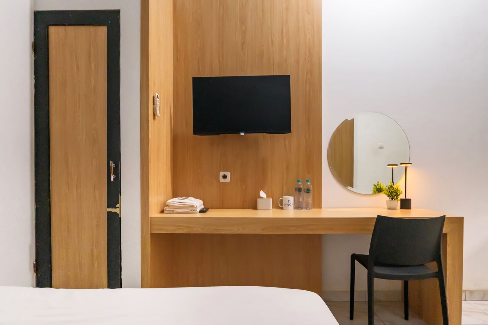 Ein Hotelzimmer mit einem Holztisch, einem Flachbildfernseher, einem runden Spiegel, einem Sessel und einem Bett.