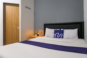 A hotel room with a bed, a nightstand, a lamp, and a wooden door. - INNCA Singa Utara, Semarang (Semarang)
