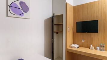 Habitación de hotel con un mueble de madera, un televisor de pantalla plana, una mesita de noche con un teléfono, pañuelos de papel y botellas de agua.